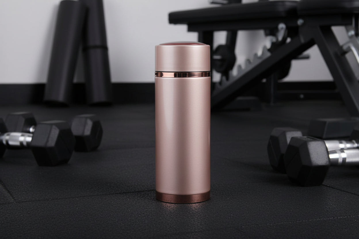 Rose gold thermos on a textured surface with a pipe in the background
